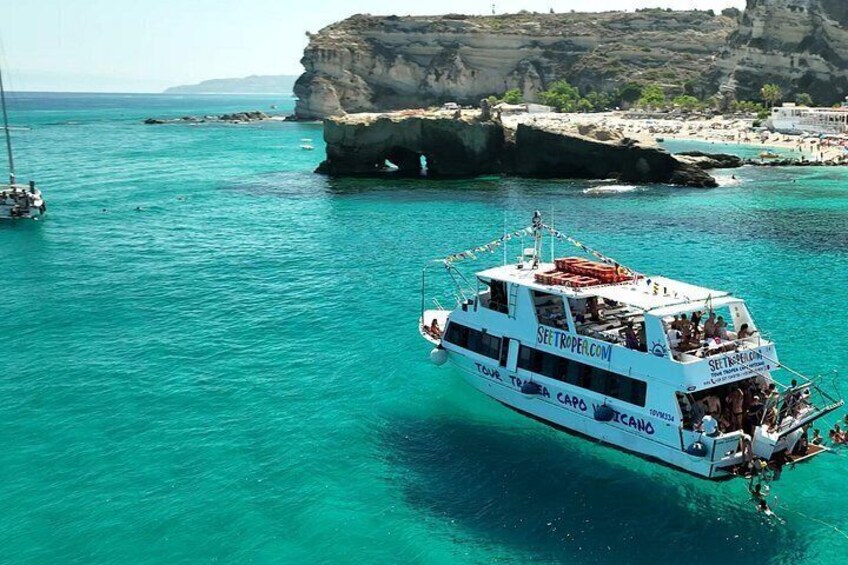 A boat named 'SEETROPE.COM' on turquoise waters with a rocky coastline in the background. 2