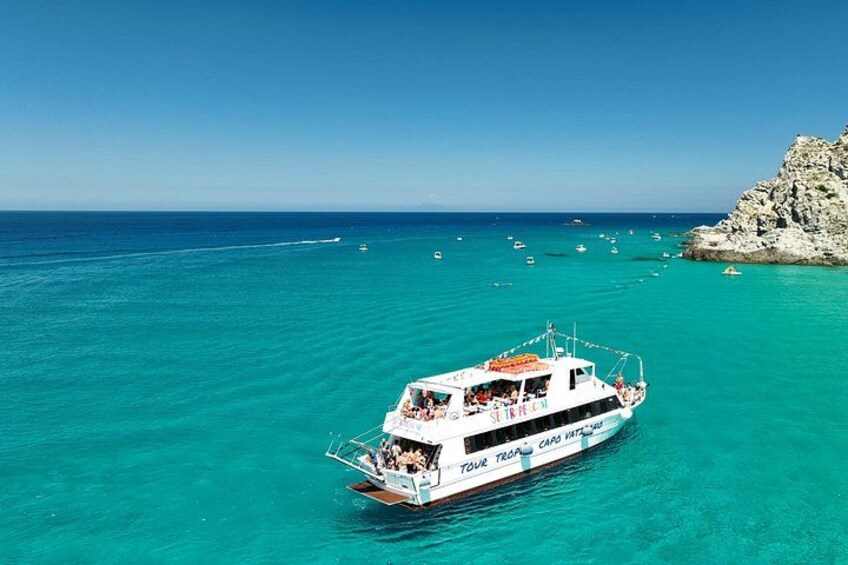A boat named 'Your Tropic Card' on turquoise waters with a rocky coastline in the background. 4