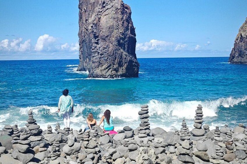 A rocky shoreline with stacked stones, calm sea, and large rock formations in the background. 2