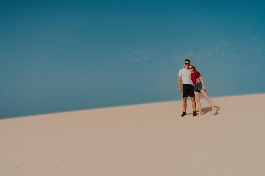 Twee personen staan op een zandduin met een strakblauwe lucht. 3