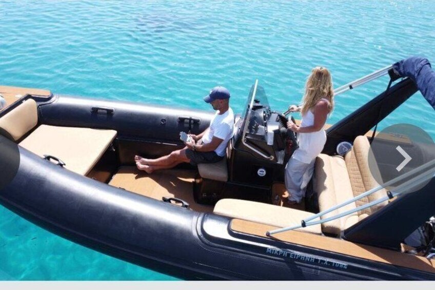 A motorboat on clear blue water with two people, one steering and one sitting. 5