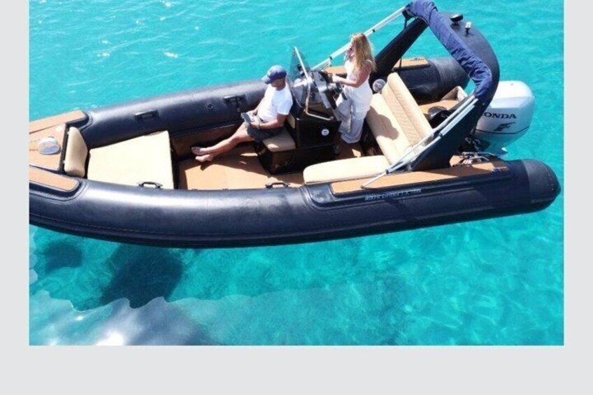 A man and a woman on a motorized inflatable boat with a Honda engine, floating on clear blue water. 1