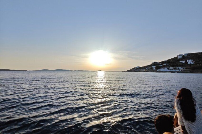 A sunset over a calm sea with a distant shoreline and white buildings. 3