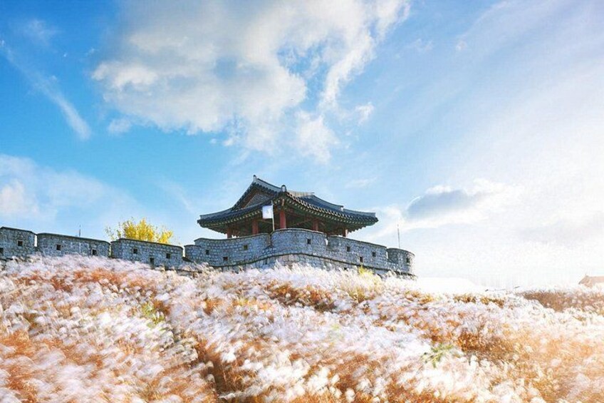 Un edificio tradicional coreano con tejado de tejas, rodeado por un muro de piedra y plantas con flores. 5