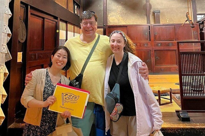 Three people in a room with wooden furniture and a yellow book titled 'Deep Essence.' 1