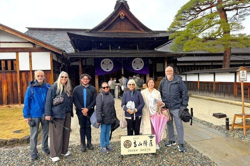 A group of people standing in front of a traditional Japanese building with a sign that reads 'Shinshu Kurokawa Hachiman Shrine'. 1