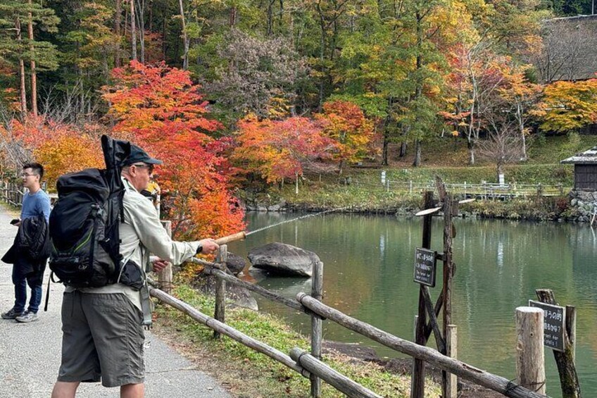 A person pointing at a sign near a lake with autumn foliage. 4