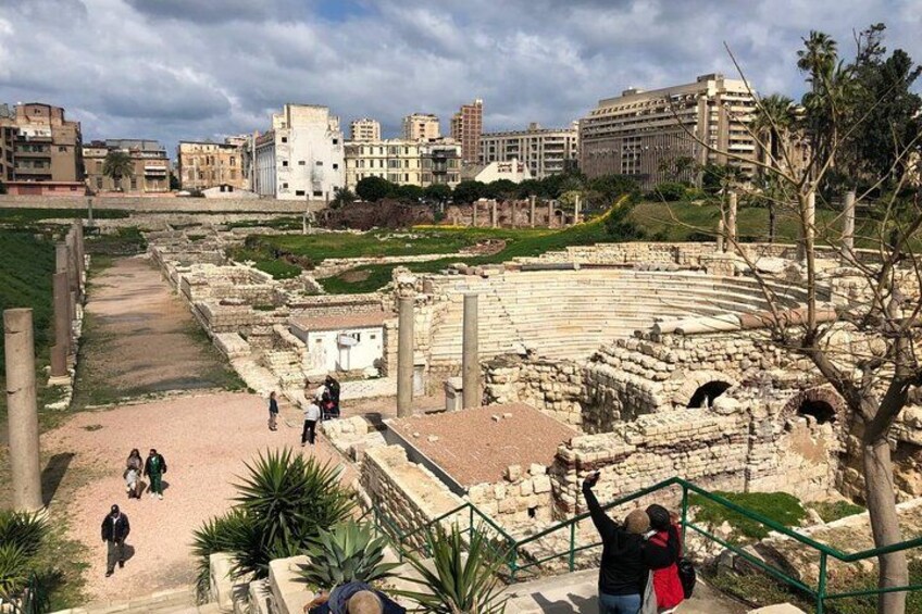 Ancient ruins with columns, a stage, and modern buildings in the background. 3