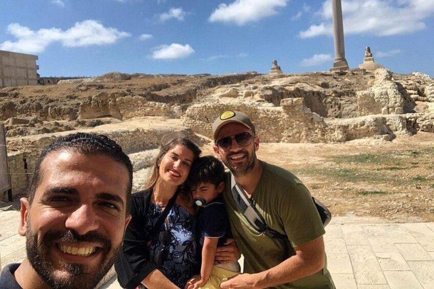 A family at an archaeological site with ancient ruins and a tall column in the background. 5