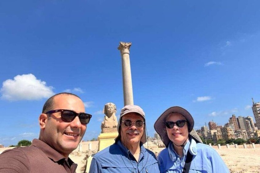 Three people standing in front of a tall column with a statue in the background. 2