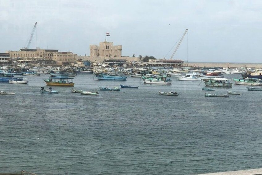 Un puerto con numerosos barcos, un edificio destacado con una bandera y grúas de construcción al fondo. 2