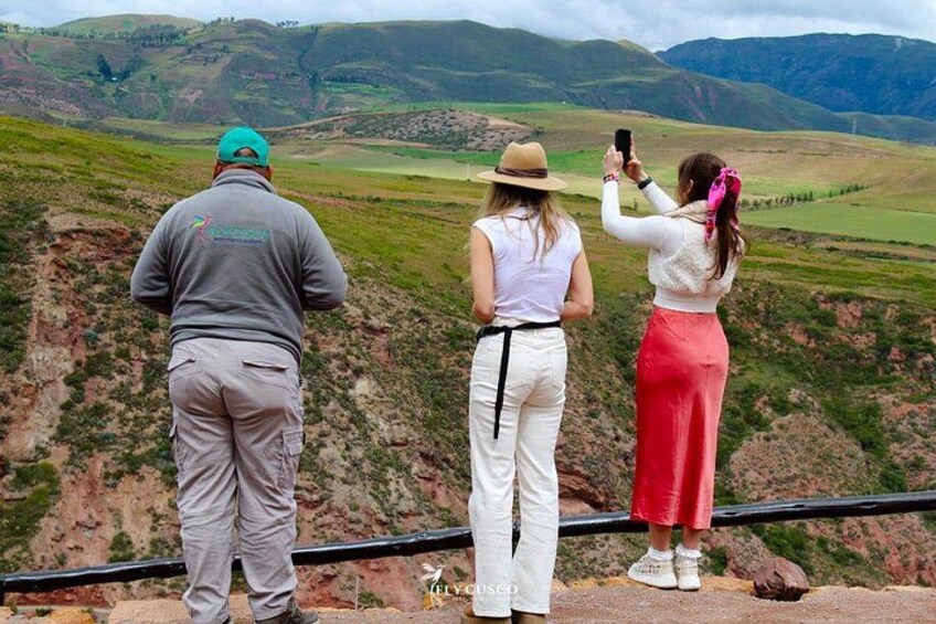 Tre persone in piedi su una sporgenza con vista su una valle, un lago e montagne sullo sfondo. 2