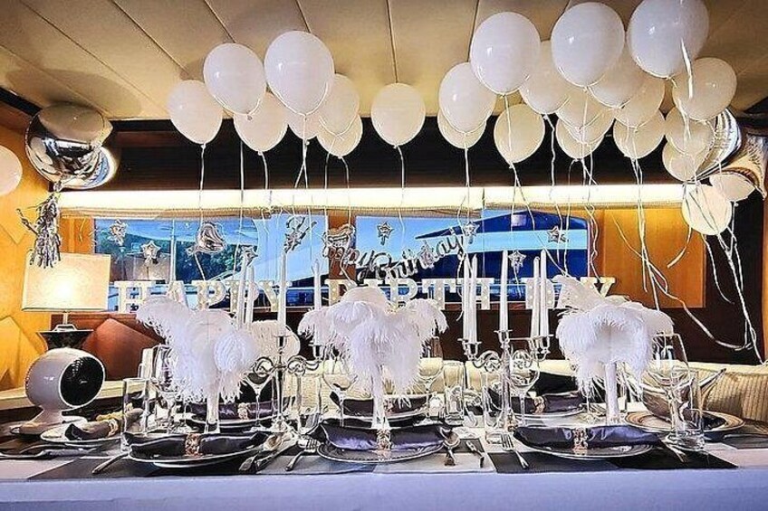 A table set for a formal event with white feathered centerpieces, balloons, and a 'Happy Birthday' sign. 3