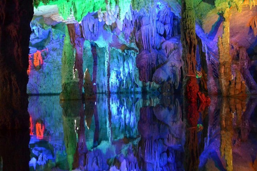 Eine Höhle mit bunten Stalaktiten und Stalagmiten sowie einer spiegelnden Wasseroberfläche. 4