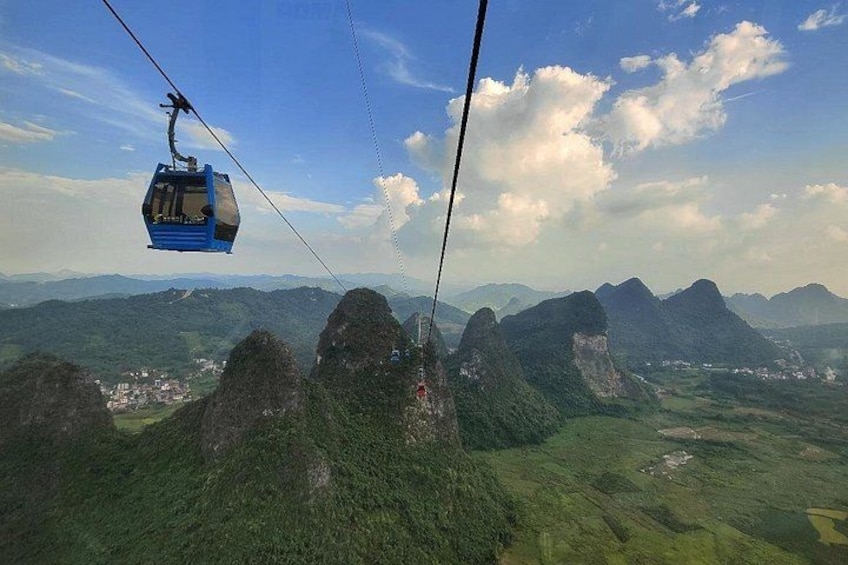 Eine Seilbahn über einer bergigen Landschaft mit üppiger Vegetation und fernen Gipfeln. 1
