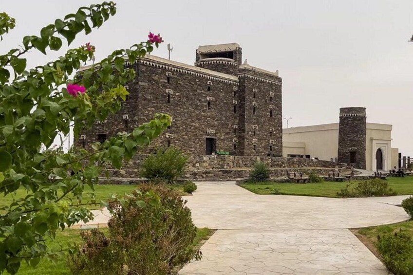 A historic stone building with a large courtyard, a smaller adjacent building, and a pathway leading to the entrance. 3