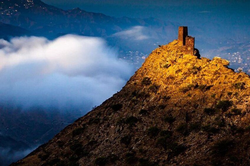 A mountain peak with a small structure on top, surrounded by clouds. 5