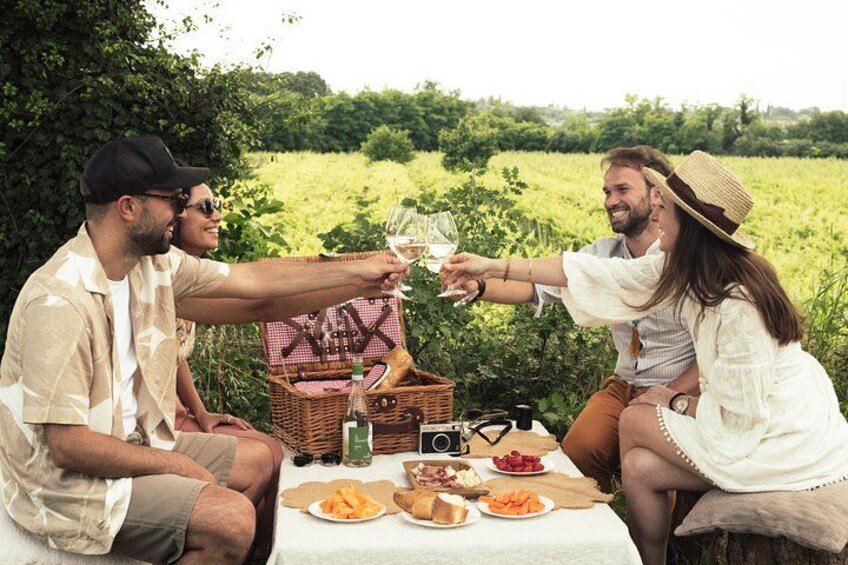 Trois personnes pique-niquent en plein air, avec un panier, des verres à vin et de la nourriture. 1