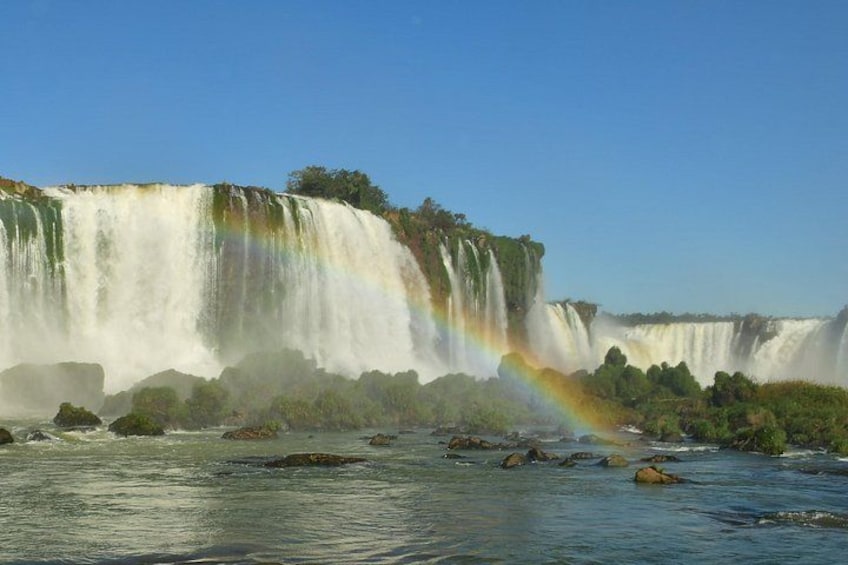 A large waterfall with a rainbow, surrounded by greenery and rocks. 3