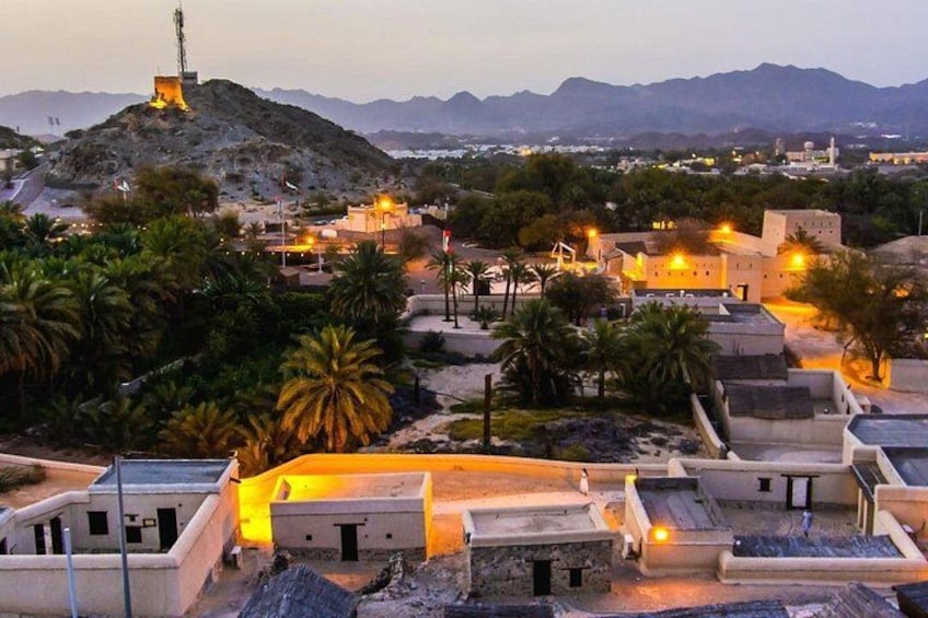 A desert landscape with buildings, palm trees, and a hill with a tower. 5
