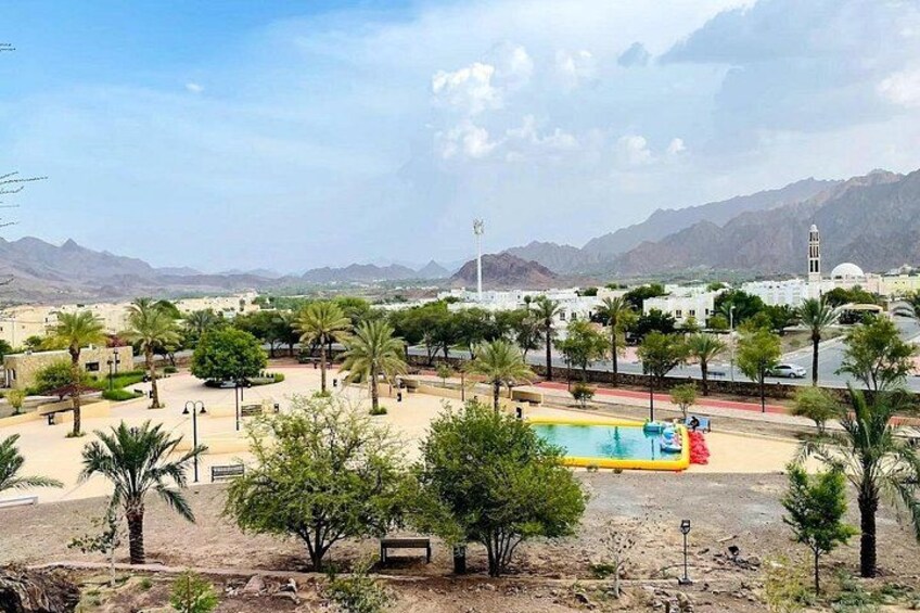 A pool area with palm trees, a clear sky, and mountains in the background. 2