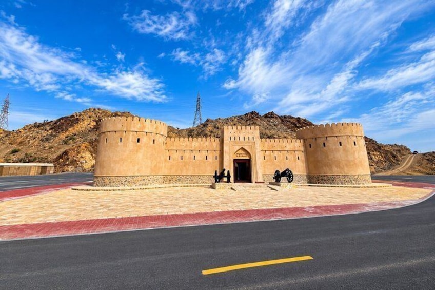 A historic fort with a large entrance gate, a paved area in front, and a clear blue sky. 2