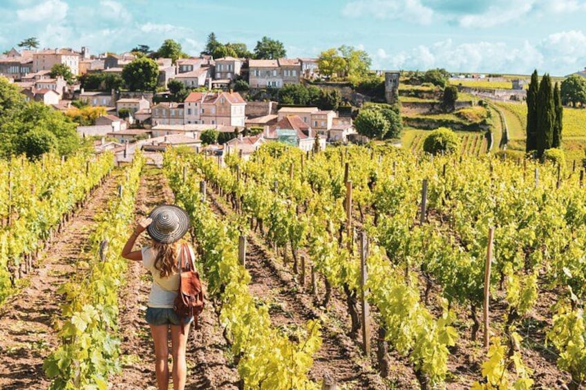 Un vignoble avec des rangées de vignes, une femme portant un chapeau et une ville en arrière-plan. 1