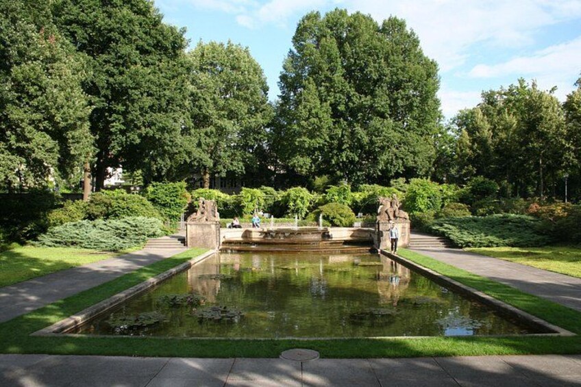 A rectangular pond with statues, surrounded by a well-maintained garden and trees. 4