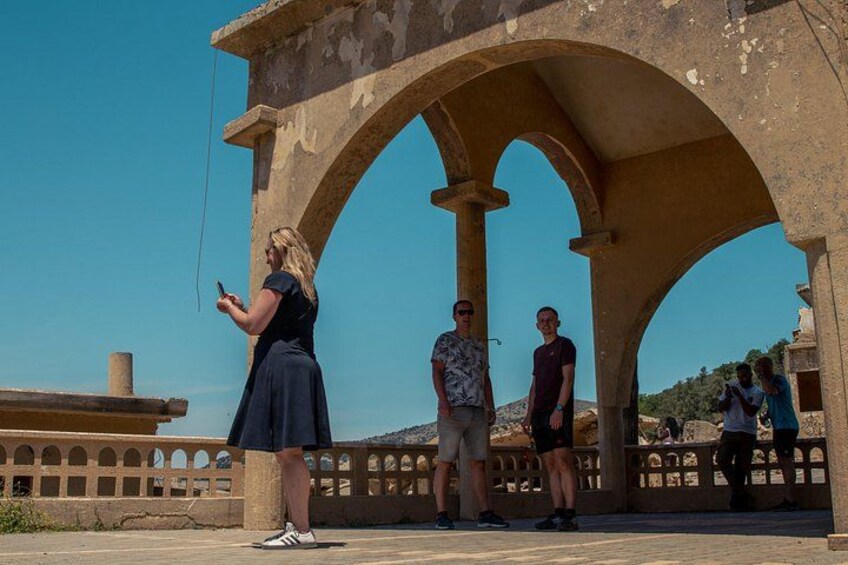 A woman using a mobile device, a man in a patterned shirt, and another man in a red shirt standing under an archway. 3