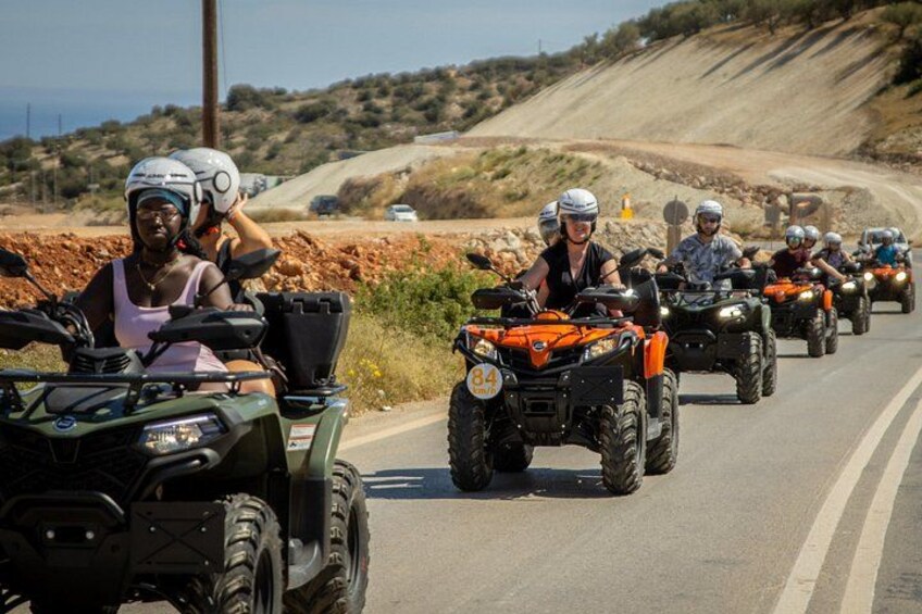 A group of people riding ATVs on a road with a hilly landscape in the background. 2