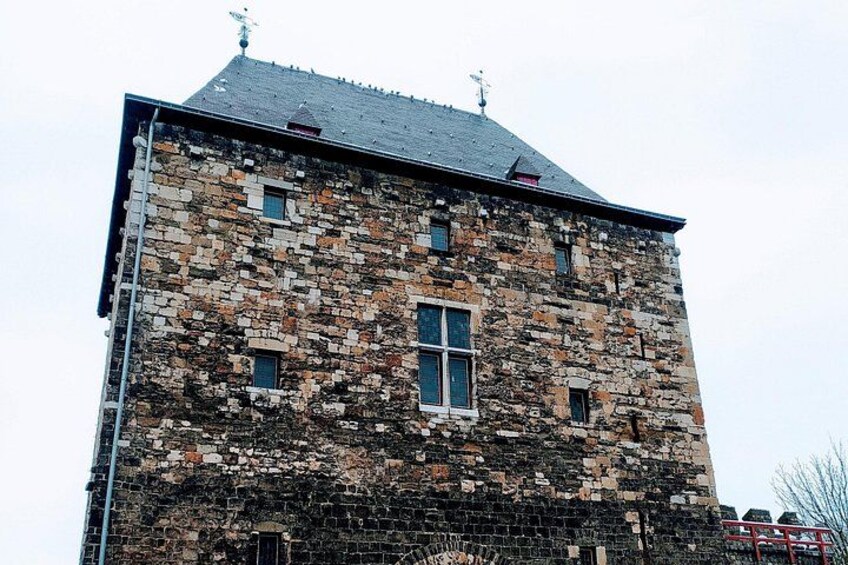 A tall, multi-story stone building with a sloped roof and multiple windows. 3