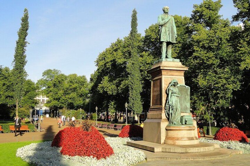 Een standbeeld in een park met rode en witte bloembedden en hoge bomen. 2