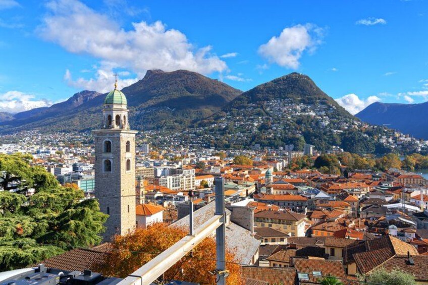 A town with a prominent tower, a mountain in the background, and a mix of red-roofed buildings. 2