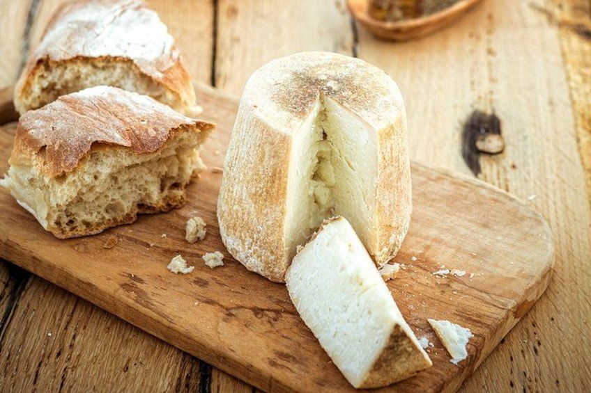 Une meule de fromage, une miche de pain et une planche à découper sur une surface en bois. 4