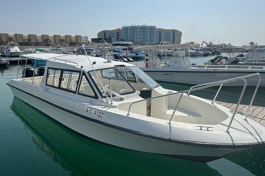 A white motorboat with the registration number AC 9727 docked at a marina with other boats and buildings in the background. 2