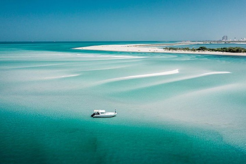 A boat on turquoise waters with a sandy beach and distant buildings. 3