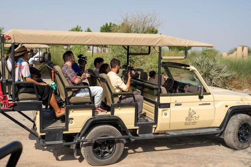 A safari vehicle with passengers, a desert landscape, and sparse vegetation. 2