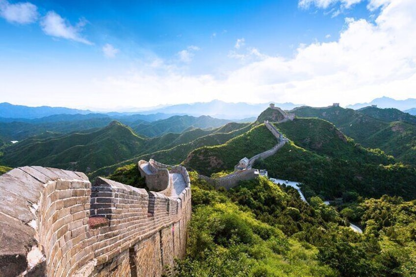 The Great Wall of China winding through lush green hills under a clear sky. 5