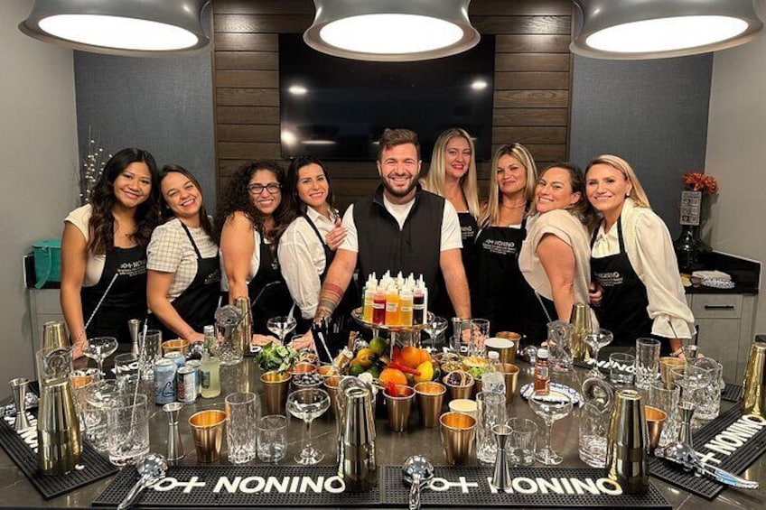 Un grupo de personas de pie alrededor de una mesa con vasos y botellas, con la palabra 'NONINO' escrita en el mantel. 2