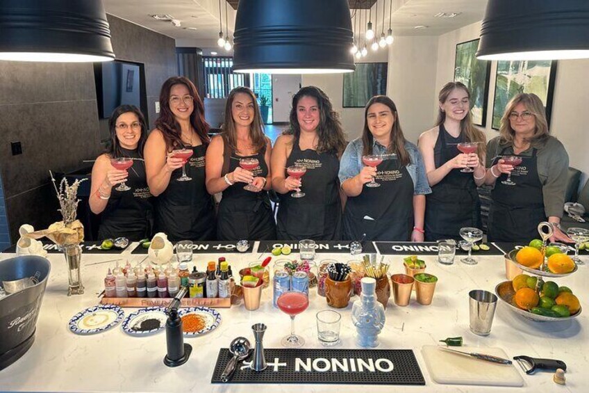A group of people in aprons holding drinks at a table with various food and drink items. 2