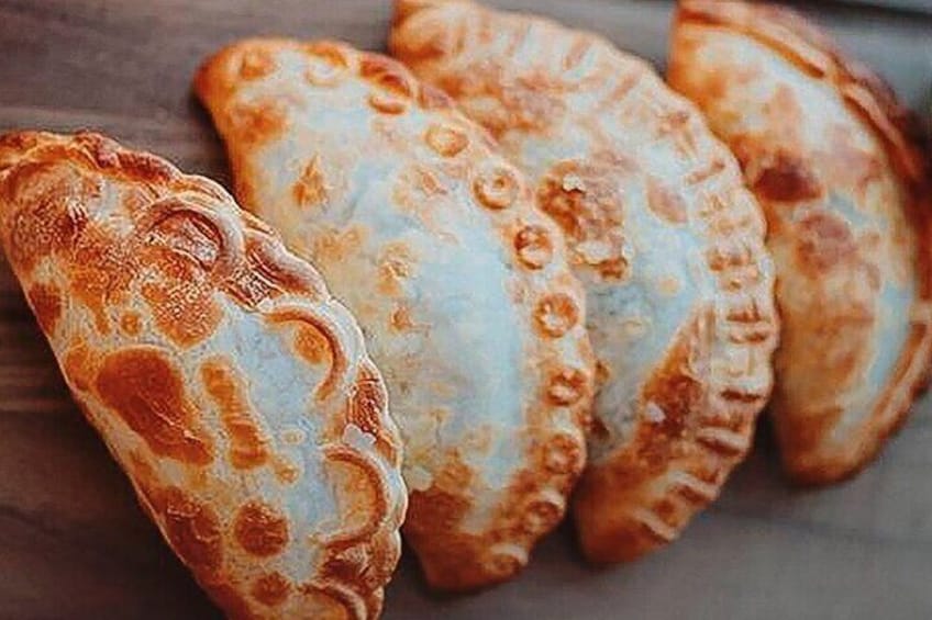 Trois pâtisseries dorées, de couleur brun clair, avec un bord ondulé, probablement des chaussons ou des empanadas, posées sur une surface en bois. 1
