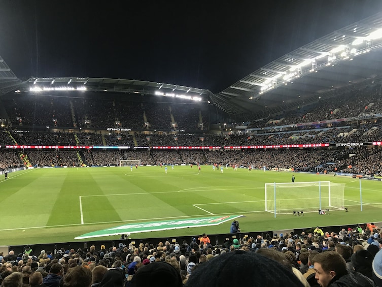 A football stadium filled with spectators, a green pitch, and goalposts. 1