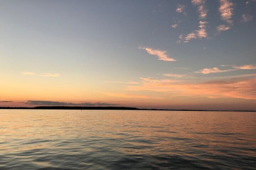 Ein ruhiges Meer bei Sonnenuntergang mit einer entfernten Küstenlinie und wolkenlosem Himmel. 2