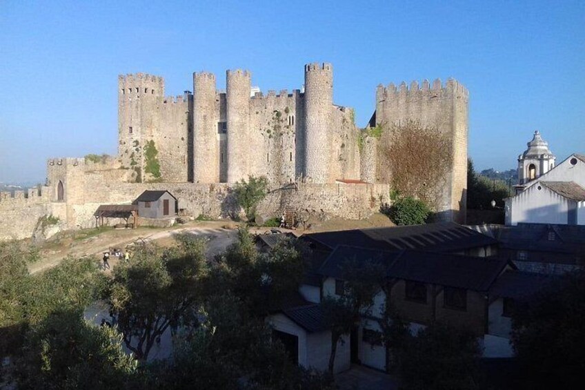 Un château historique doté de nombreuses tours et entouré de remparts, situé dans une ville où se côtoient bâtiments et espaces verts. 1
