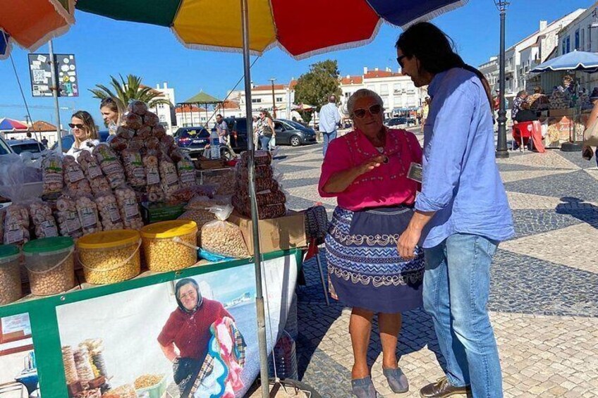 Un marché de rue avec des étals de nourriture, des gens qui font leurs courses et un trottoir pavé. 4