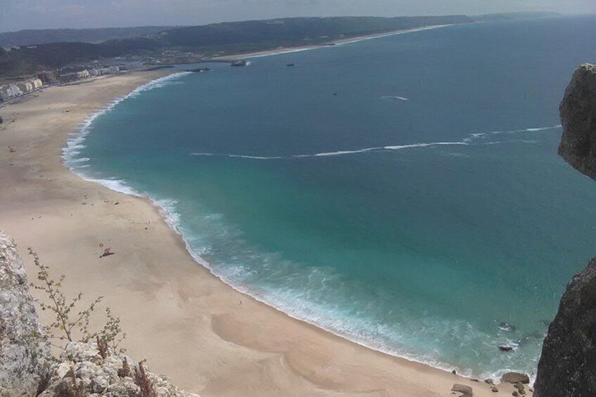 Un paysage côtier caractérisé par une plage de sable, des eaux turquoise et limpides, et un promontoire rocheux. 3