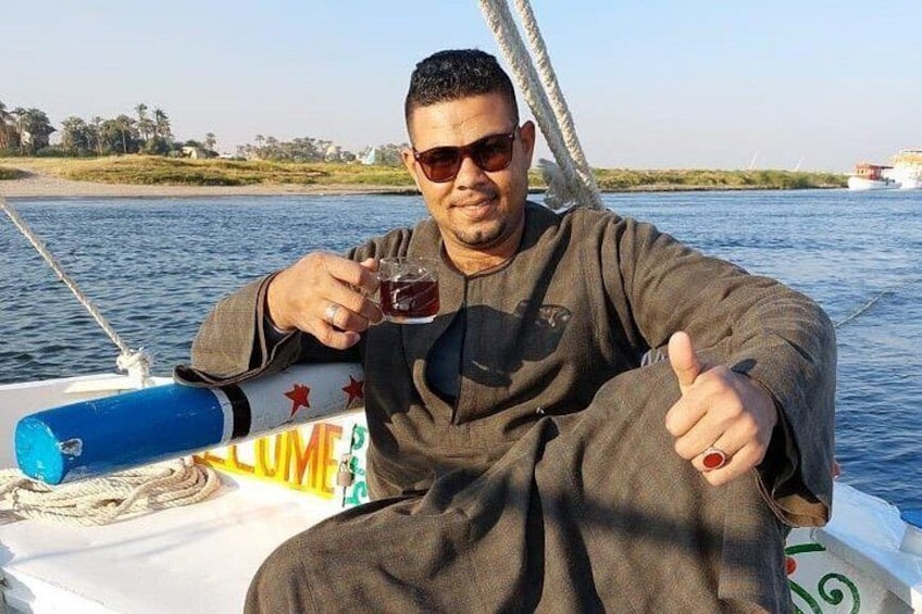 Una persona seduta su una barca, con un drink in mano, con un corpo d'acqua e una costa in lontananza. 4