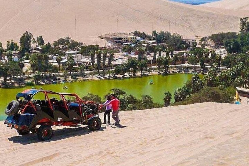 A dune buggy on a sandy hill, a body of water, and a distant town. 5