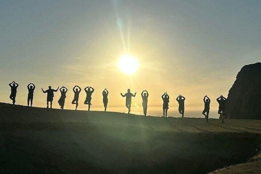 Silhouettes of people performing yoga poses on a beach at sunset. 4