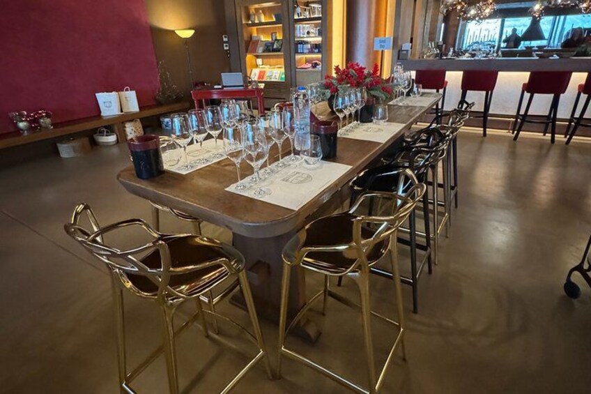 Un bar con una larga mesa de madera, sillas de metal y una barra con taburetes. 5